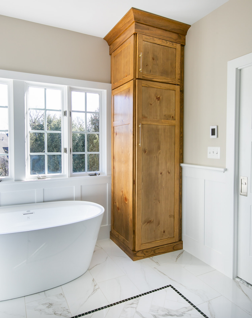 A tall custom wooden storage cabinet installed in a renovated bathroom by TCS Woodworking in Baltimore, MD