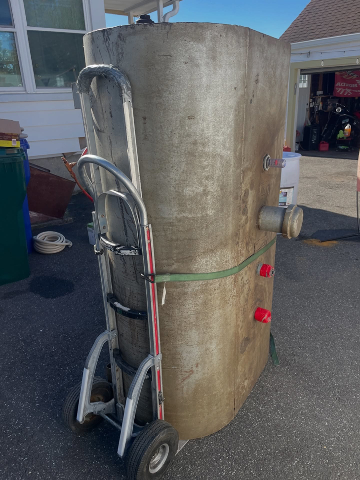 A tall, cylindrical tank secured to a hand truck, being moved for removal by DLS Junk Removal in Waterbury, CT.