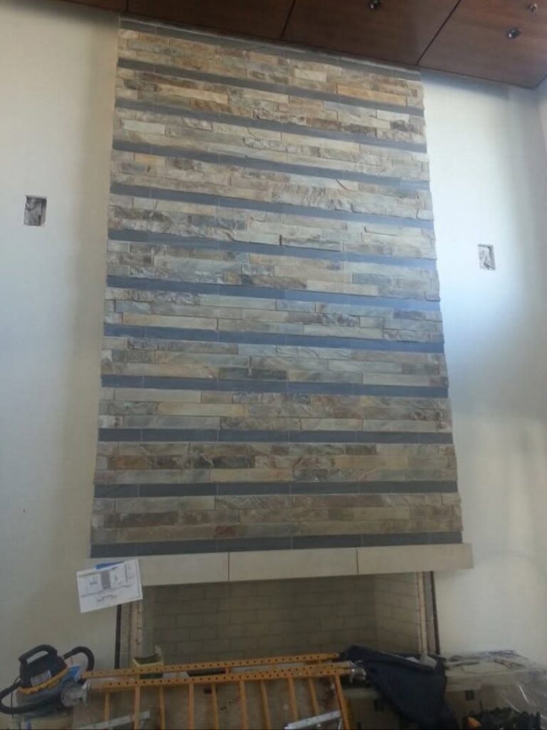 A tall fireplace wall with horizontal stone tiling, showing a construction site by Infinite Fire Features in Colorado Springs, CO.