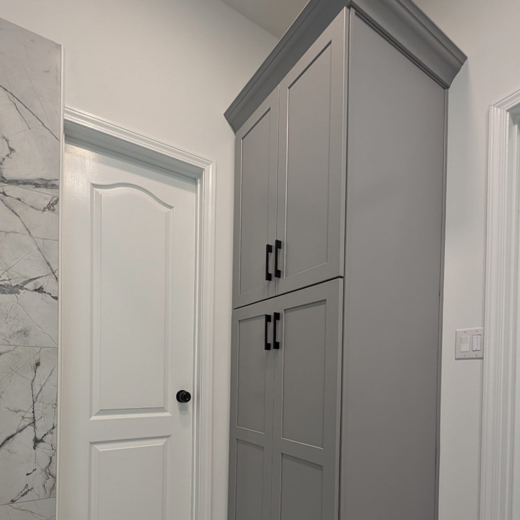 A tall gray bathroom linen cabinet with black handles installed by Ensotile - Atlanta Bathroom Remodeling in Stone Mountain, GA