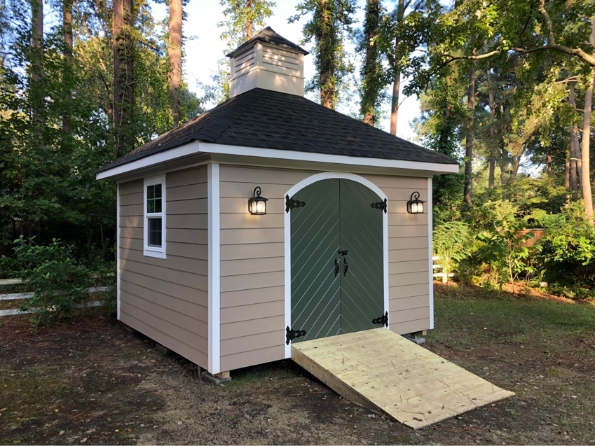 A tan shed featuring unique arched green doors and a decorative cupola, built by RMG Construction in Chesapeake, VA.