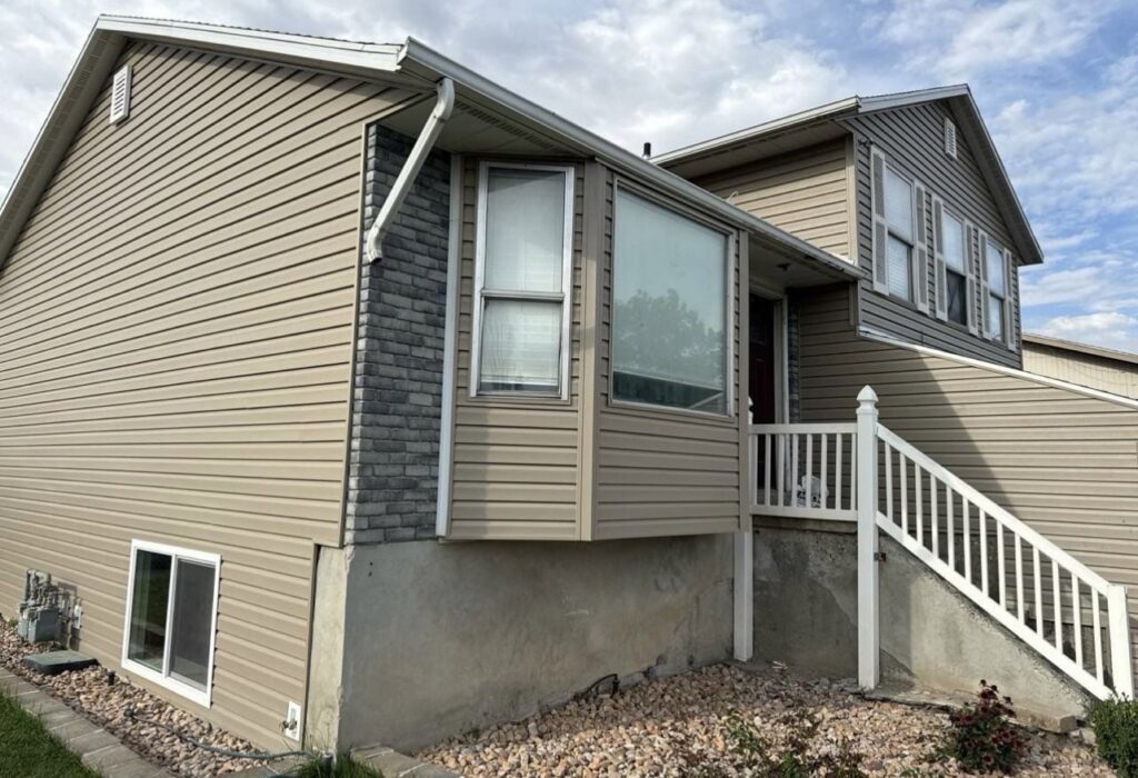 A house with new tan siding and decorative stone accents, showcasing a completed exterior by Ideal Siding Richmond, VA.
