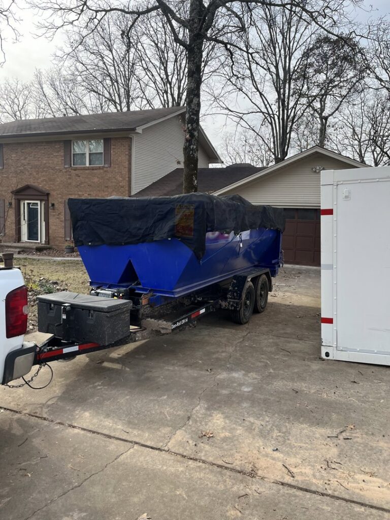 A blue dump trailer with a black tarp covering its contents, parked in a driveway by Primo Operations in North Little Rock, AR.