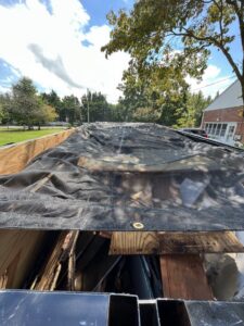 A Trademark Dumpsters trailer filled with wood debris and covered by a tarp after a junk removal job in Wilmington, DE.
