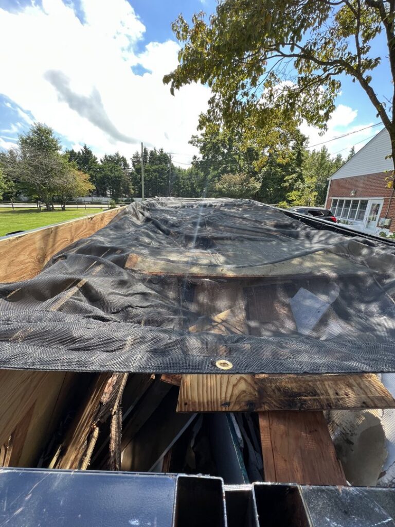 A Trademark Dumpsters trailer filled with wood debris and covered by a tarp after a junk removal job in Wilmington, DE.