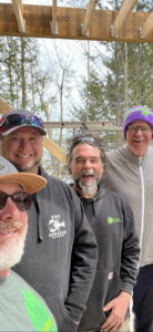 The J & J Custom Builders LLC team smiling at a construction site with exposed wooden beams in Milford, CT.