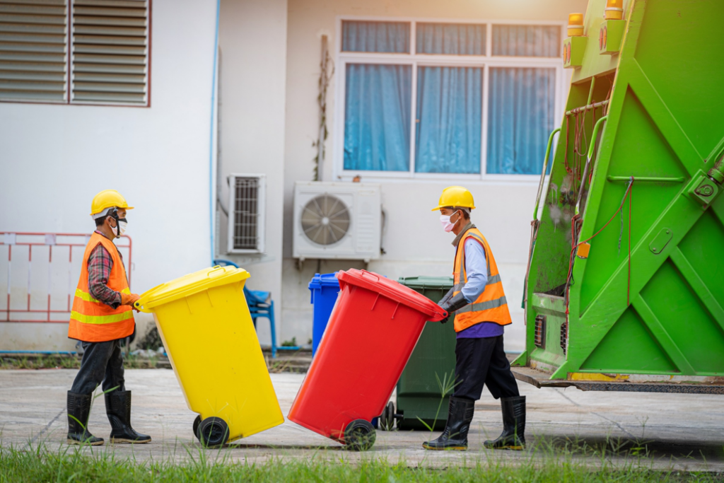 A JUNK Monster team hauling waste bins to a green garbage truck in Santa Ana, CA.