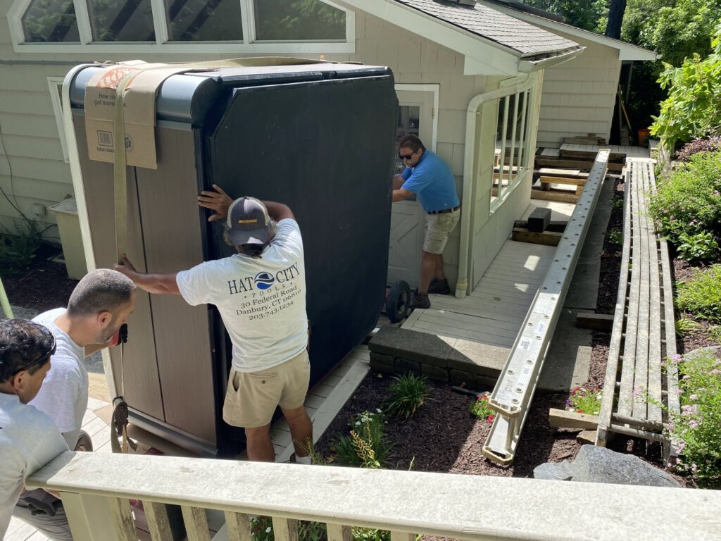 A team from Hat City Pools installing a hot tub, moving it upright on a dolly in Danbury, CT