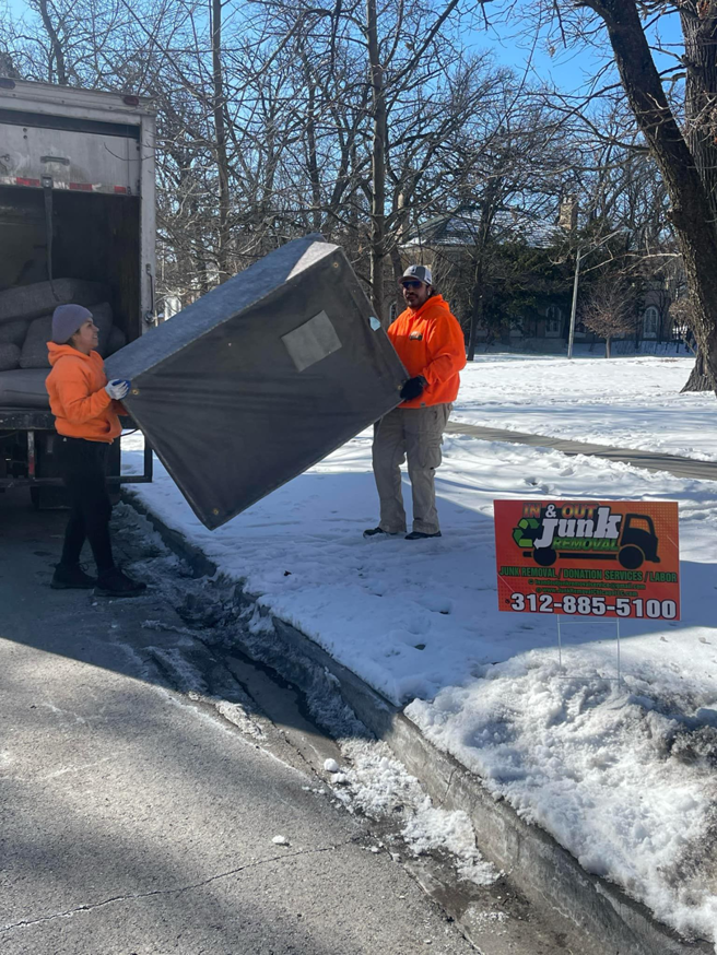 A team loading a box spring into a junk removal truck with an In & Out Junk Removal Service LLC sign in Chicago, IL.