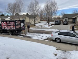 Hagen's Junk Removal team members loading items into a junk removal truck on a snowy residential street in Fort Collins, CO.
