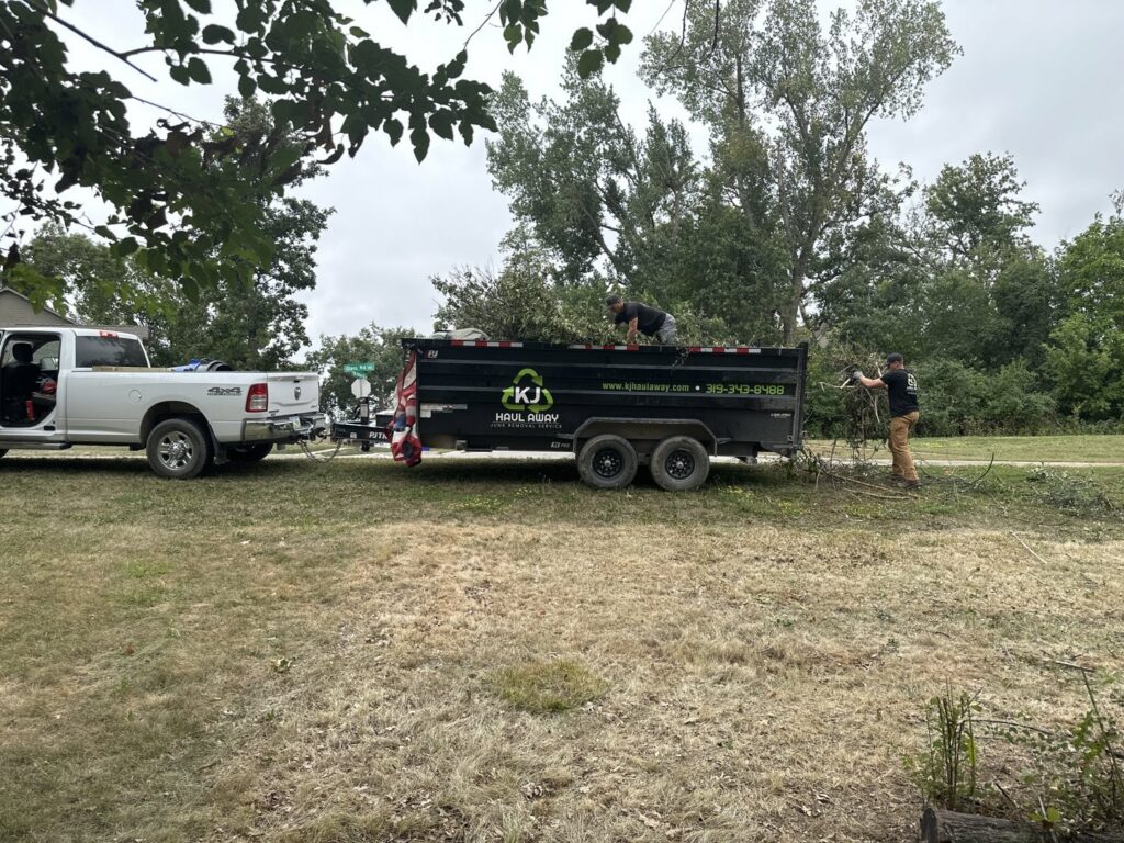 KJ Haul Away Junk Removal team members loading yard debris and brush into a branded dump trailer in Cedar Rapids, IA.