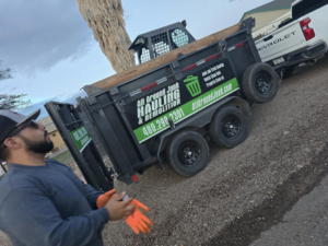 A team member putting on gloves next to a branded dump trailer from ALL around junk, LCC, preparing for a job in Mesa, AZ.