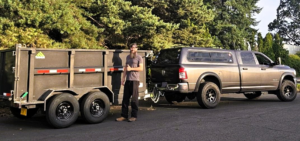 A team member standing proudly next to a pickup truck and dump trailer, ready for a junk removal job with Pacific Cascade Junk Removal LLC in Portland, OR.