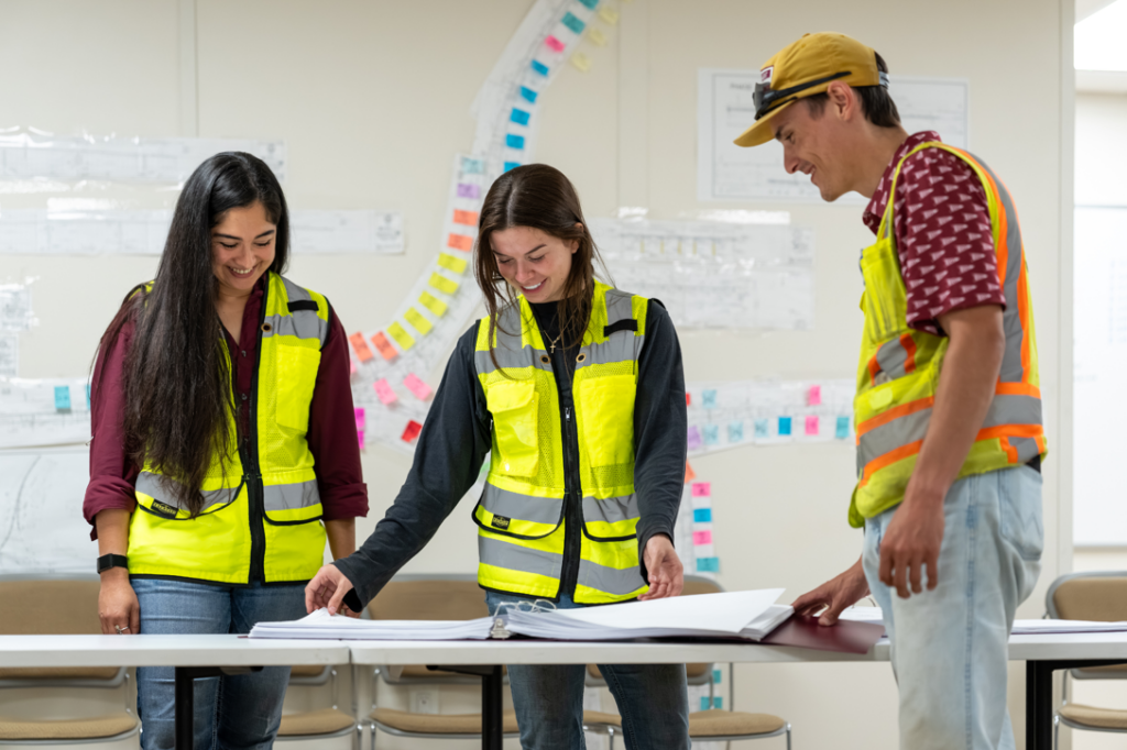 A team of construction professionals in safety vests reviewing blueprints and plans at Zachry Construction Corporation in San Antonio, TX.