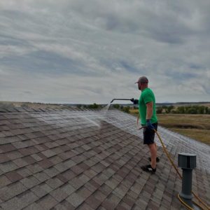 A technician applying a rejuvenating roof treatment to asphalt shingles for Roof Maxx of S Aurora, CO
