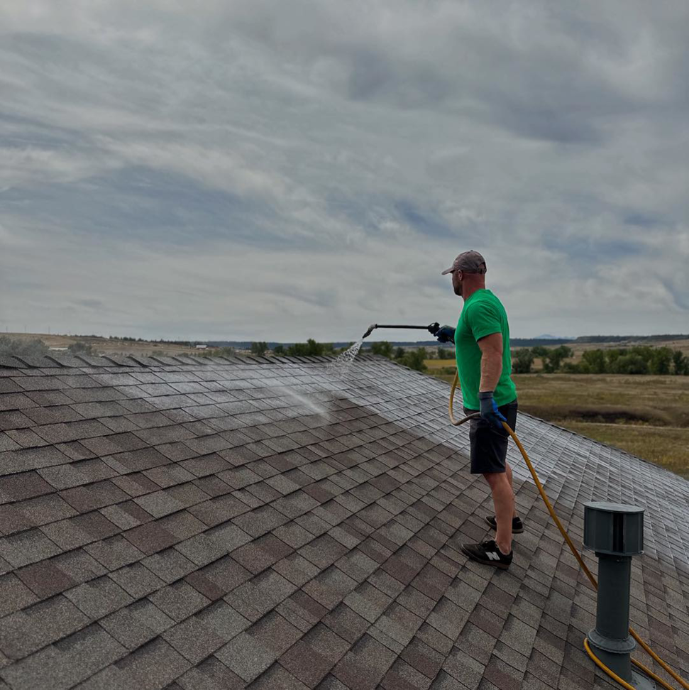 A technician applying a rejuvenating roof treatment to asphalt shingles for Roof Maxx of S Aurora, CO