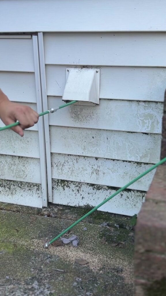 A technician from Dryer Vent Cleaning of Delaware using a cleaning rod to clear an exterior dryer vent in Wilmington, DE.