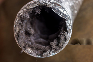 A SafeVent Dryer Vent Cleaning technician uses a power tool to clean a dryer vent opening in a wall in Wilmington, NC.