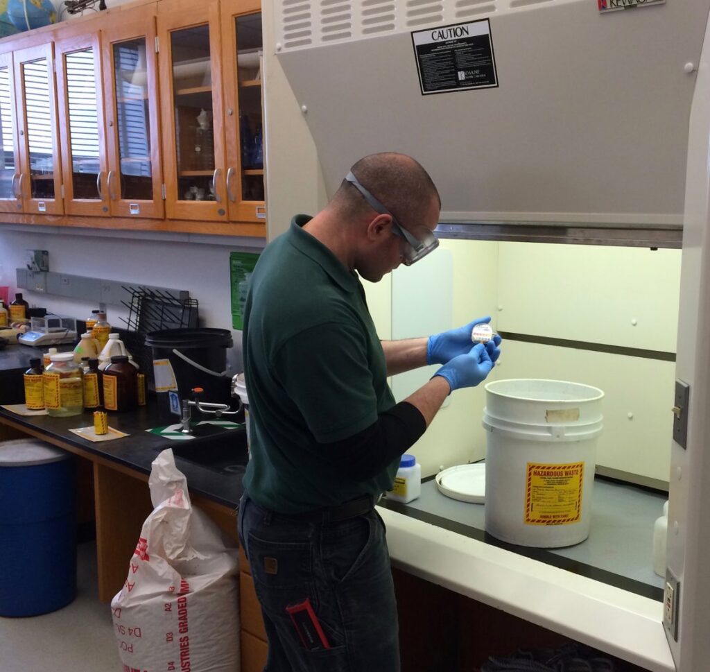 A technician in safety gear processing hazardous waste under a fume hood for MLi Environmental in South Portland, ME.