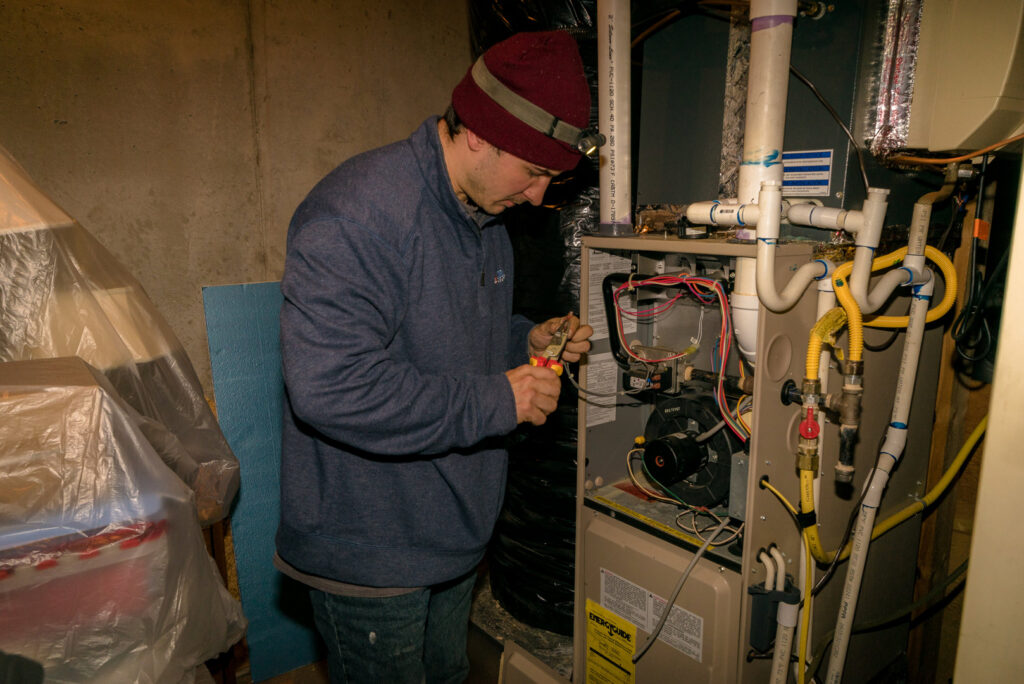 A technician from Cool Change Heating & Air repairing an indoor furnace unit in a basement in Raleigh, NC.