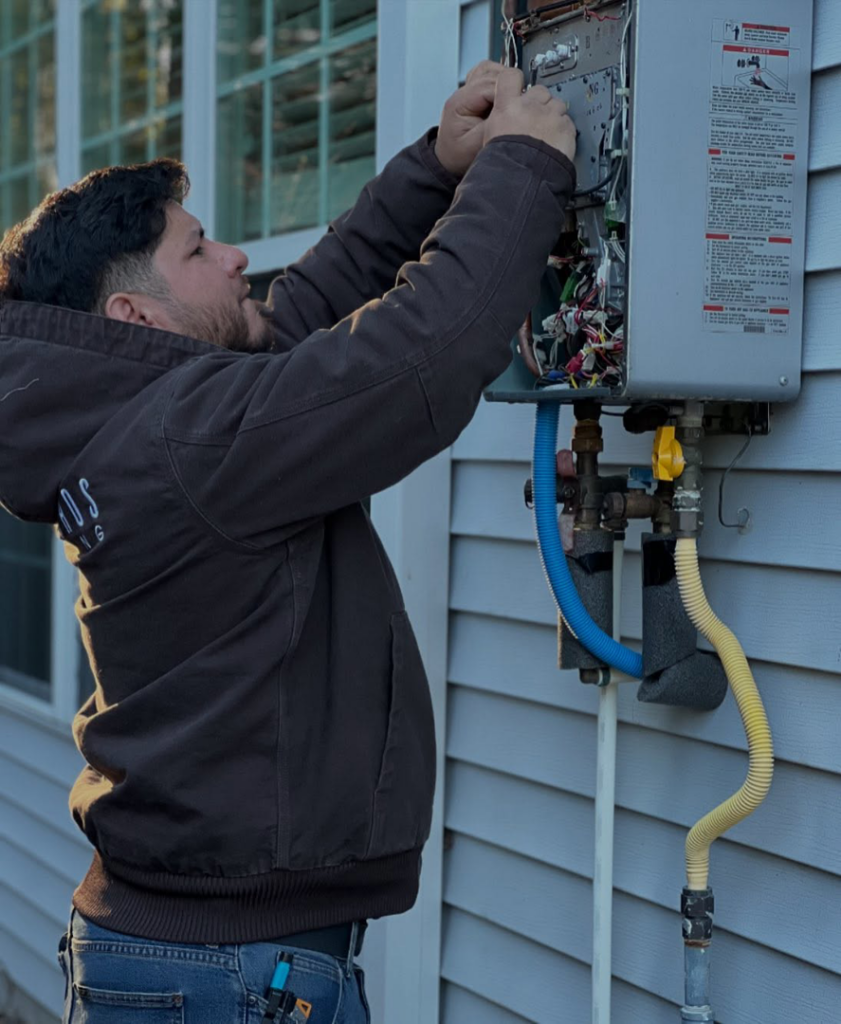 A technician repairing an outdoor tankless water heater for Sandobros Plumbing in Charleston, SC