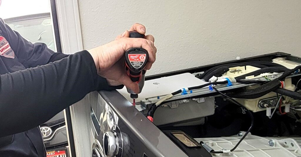 A technician from Appliance Handyman of Twin Falls, ID, using a power drill to repair a washing machine