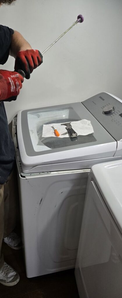 A technician from Appliance Handyman of Twin Falls, ID, servicing a top-load washing machine with specialized tools