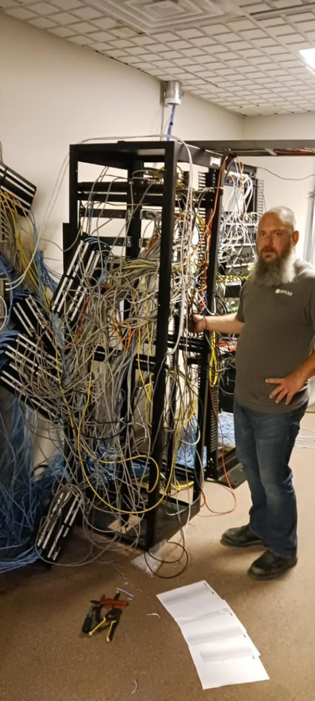A technician from Home Run Cabling & Technologies in Madison, WI, standing next to a server rack with tangled cables, ready for organization.