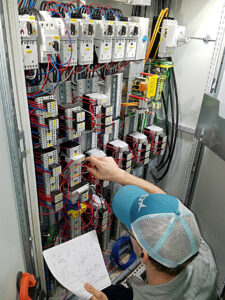 A technician working on a complex electrical control panel with a wiring diagram for Joyner Electric And Security in Savannah, GA.