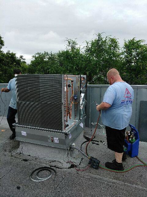 Two technicians installing or repairing a large HVAC unit on a rooftop for Our Place Air & Home Repair in Orlando, FL.