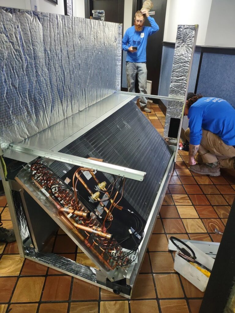 Two technicians installing or repairing a large commercial HVAC unit indoors for Pollock HVAC & Electrical in Albany, GA