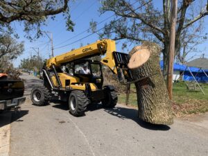 A telehandler lifting a large section of a tree trunk from a street during a tree removal job by Tri-County Tree And Restoration in Jackson, MS.