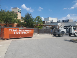 An orange Texas Dumpstars dumpster placed for rental in a parking lot in Hutto, TX.