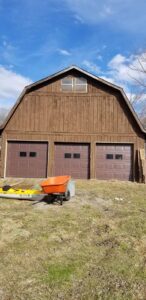 Three matching brown garage doors installed on a rustic barn by Lucas Overhead Doors in Erie, PA.