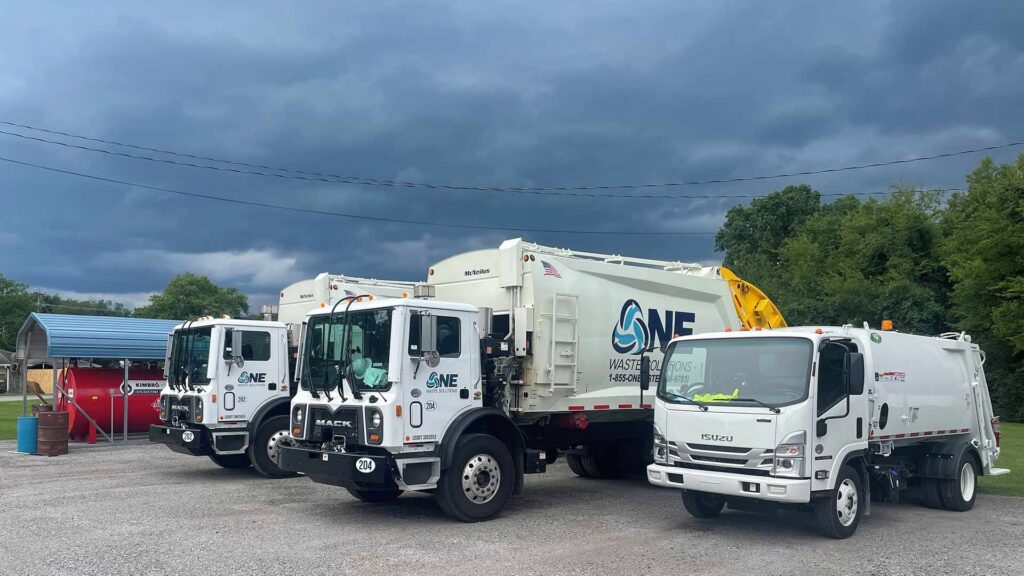 Three white garbage trucks from One Waste Solutions parked under a cloudy sky in Murfreesboro, TN, ready for junk removal services.