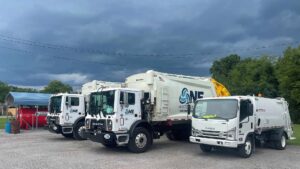Three white garbage trucks from One Waste Solutions parked under a cloudy sky in Murfreesboro, TN, ready for junk removal services.