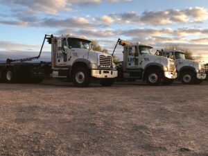 Three roll-off trucks from Liberty Disposal, Inc. parked in a lot at sunset in Tucson, AZ.