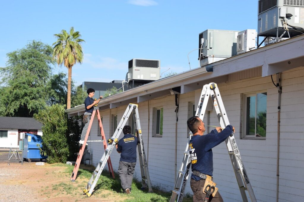 Three workers from Phoenix Rain Gutters and Sun Protection on ladders installing rain gutters on a commercial building in Glendale, AZ.