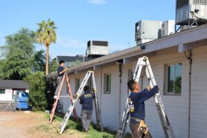 Three workers from Phoenix Rain Gutters and Sun Protection on ladders installing rain gutters on a commercial building in Glendale, AZ.