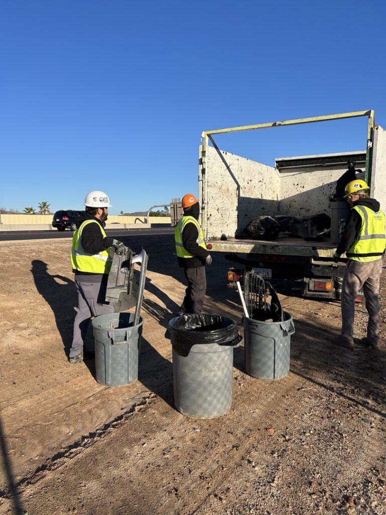 Three workers from Skunky's Junk Removal loading debris and trash cans into a truck in Tempe, AZ.