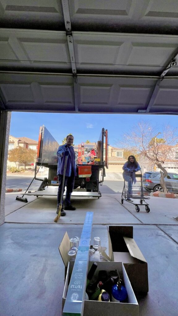 Two Tidy Toss Las Vegas, NV team members in a garage with their junk removal truck visible outside.