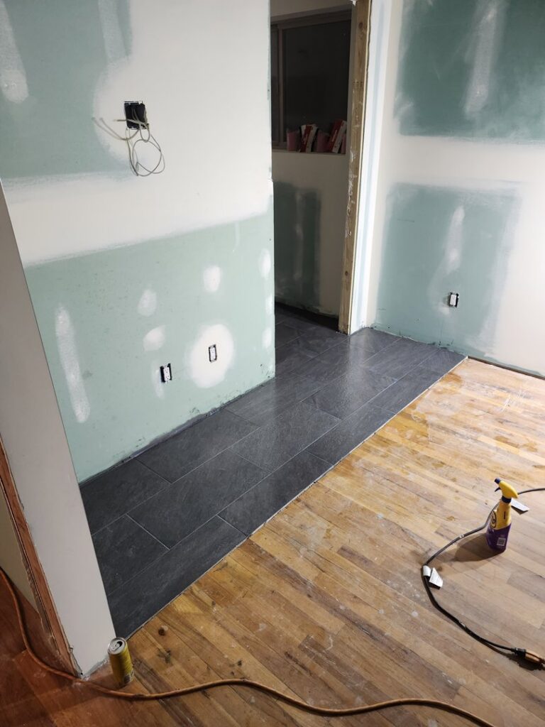 New tile flooring being installed next to wood flooring, with drywall work in progress, by Joe's Handyman Solutions in Ogden, UT.