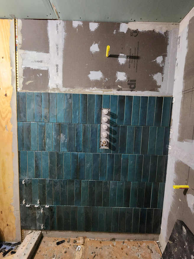 Teal subway tiles being installed on a bathroom wall during a renovation by AJAC Restore&Construct LLC in Houma, LA.