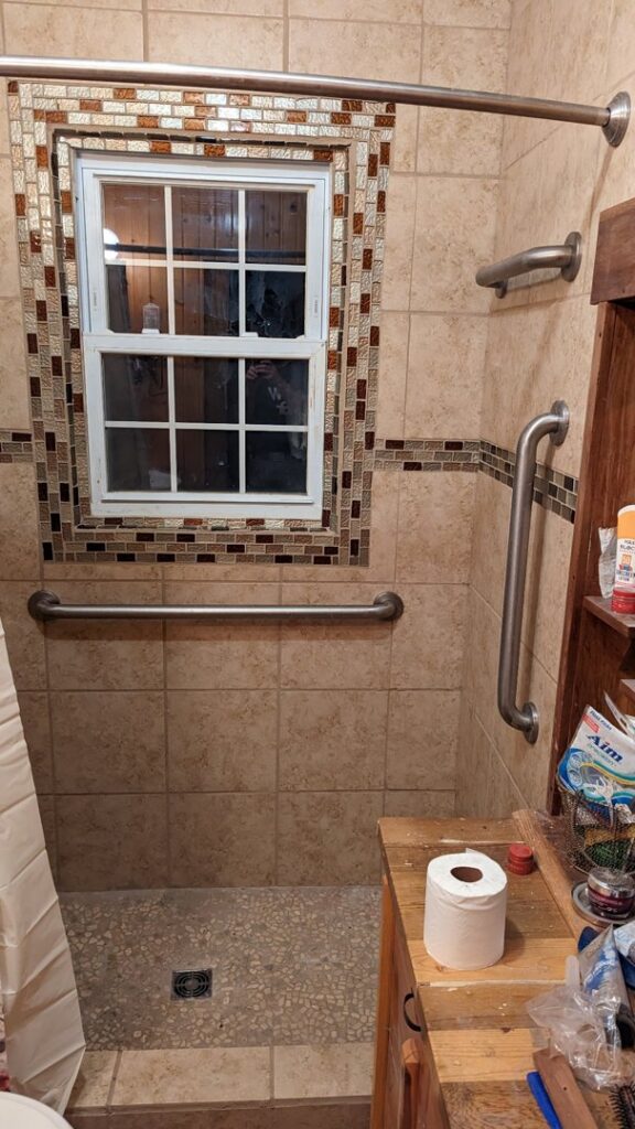 A newly tiled bathroom shower with grab bars and a decorative window, completed by Devil Dog Services LLC in Billings, MT.