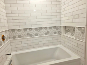 A tiled bathtub surround featuring white subway tiles and a floral accent strip by Tyler the Tiler in Jefferson, WI.