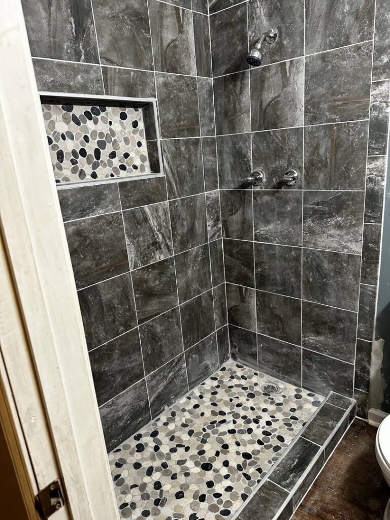 Tiled shower with pebble floor and niche during a bathroom remodel by KG Handyman & Remodeling in Vilonia, AR.