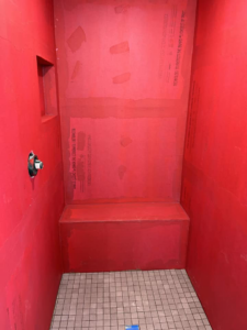 A shower with a tiled floor, built-in bench, and red waterproofed walls by G-P Construction in Springfield, OR.