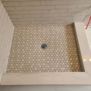 A close-up view of a newly tiled shower floor with hexagonal tiles and subway wall tiles by Stonehedge Construction in Buford, GA
