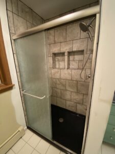 A newly installed tiled shower with a glass sliding door and black shower pan by Coastal Home Improvements in Greenwood, DE.
