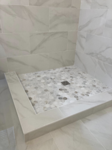 A newly tiled shower pan with hexagonal floor tiles and marble-look wall tiles from J.C.Improvement in Katy, TX.